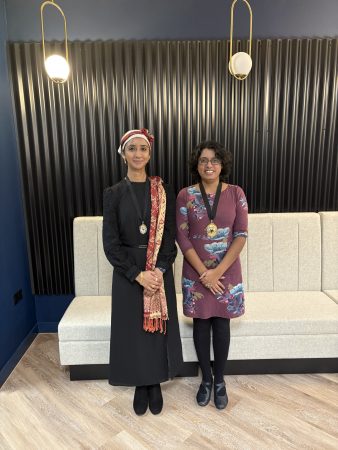 Image Description: Two women from Bristol Law Society Executive Council standing in front of a modern black-panelled wall with decorative lighting with the president and vice president wearing presidential gongs around their necks. A light-coloured bench is behind them on a wood-patterned floor.